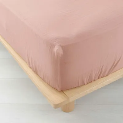 A close-up shot of a pink fitted sheet on a wooden bed frame.