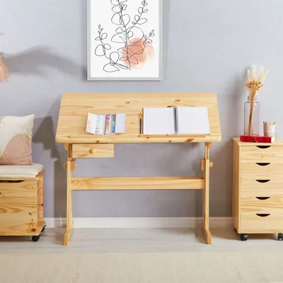 A wooden children's desk with adjustable height and tilt, placed in a room with a grey wall and a storage chest next to it.