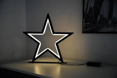 A star-shaped LED lamp sits on a white surface, with a framed picture on the wall behind it.