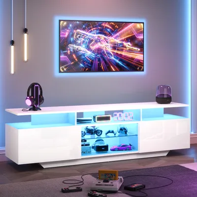 A modern living room setup featuring a white high-gloss TV stand with integrated LED lighting, a large flat-screen TV displaying a colorful abstract image, and various gaming accessories.