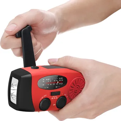 Hands holding a red and black multi-function emergency radio with a hand crank.