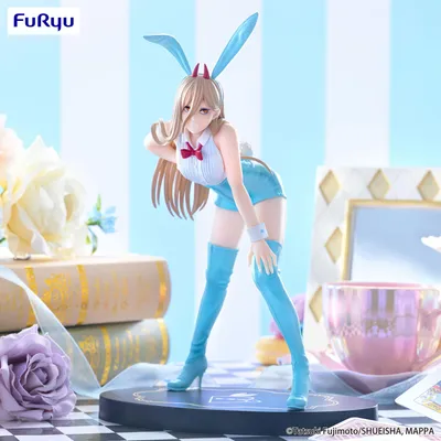 A figurine of a character in a bunny outfit is displayed on a checkered surface with decorative elements like books and a teacup in the background.