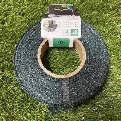 A roll of green garden tape on a spool, placed on artificial grass.