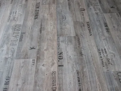 A close-up view of a wood-look vinyl flooring with text printed on it.