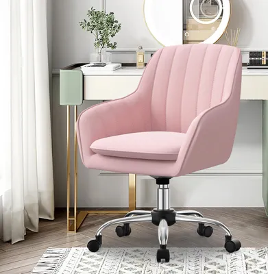 A pink velvet office chair with a silver base and wheels is shown in a room with a vanity table and curtains.