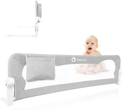 A baby is peeking over a grey bed rail on a white background.