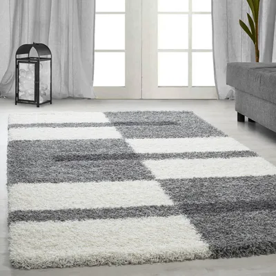 A shaggy rug with a geometric pattern in gray and white is laid out on a light gray floor in front of a doorway with sheer curtains.