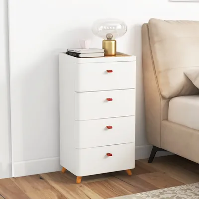 A white nightstand with four drawers and red handles, placed next to a bed.