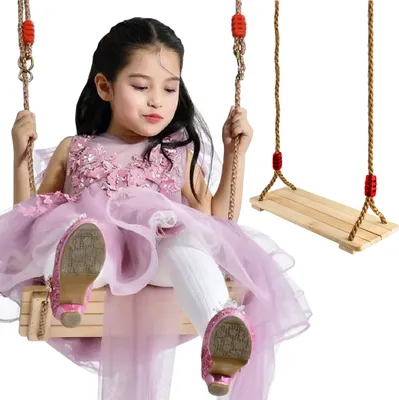 A young girl is sitting on a wooden swing, wearing a pink dress and white tights.