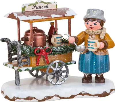 Ein fröhliches Winterkind in warmer Kleidung steht neben einem festlich geschmückten Punschwagen mit dampfendem Kessel und Tassen in der Hand bereit um heißen Punsch auszuschenken während Schnee auf dem Dach des Wagens liegt