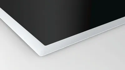 A close-up view of the corner of a black induction hob with a silver metal trim.