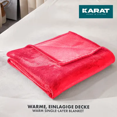 A folded red blanket is placed on a white surface, likely a bed.