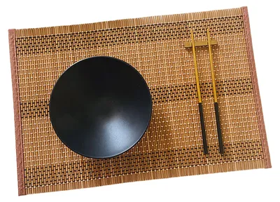 A black bowl and chopsticks are placed on a bamboo placemat.