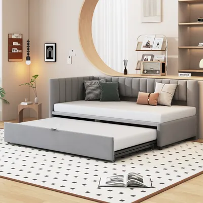 A gray daybed with a pull-out trundle bed is shown in a room with a patterned rug.