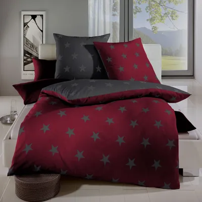 A bed with red and gray star-patterned bedding is displayed in a room with a window showing a mountain landscape.