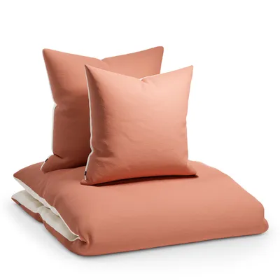 A stack of bedding, including a duvet cover and two pillowcases, in a coral color with white trim, is presented against a white background.