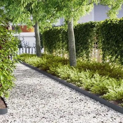 A garden path lined with white gravel and bordered by anthracite edging, with lush green bushes and trees.