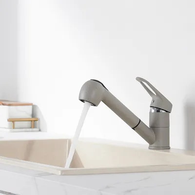 A close-up shot of a gray kitchen faucet with water running into a light-colored sink.