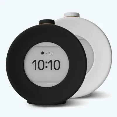 Two round alarm clocks, one black and one white, are shown against a white background. The black clock is in the foreground and displays the time 10:10 and an alarm icon with the time 7:40.