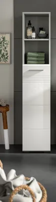 A tall, white, high-gloss bathroom cabinet with two open shelves at the top and a closed cabinet below, set against a dark gray tiled wall. A small wooden stool with a white base is to the left, and a basket of laundry is in the foreground.