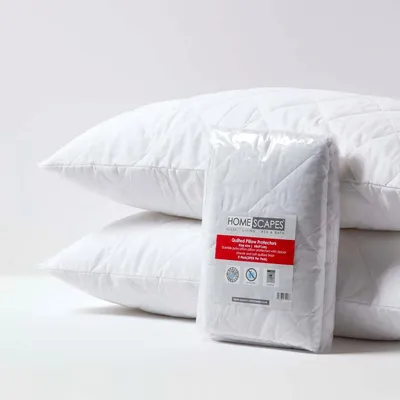 Two white quilted pillows are stacked, with a packaged set of pillow protectors in front of them.