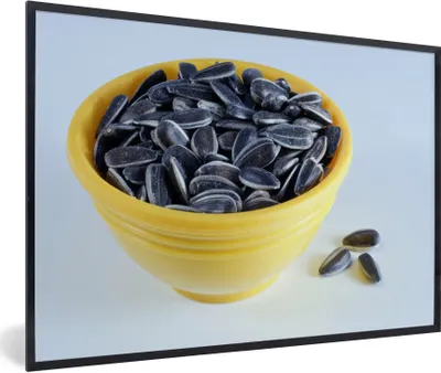 Produktbild von MuchoWow® Gerahmtes Poster Sonnenblumenkerne in einer gelben Schale mit ein paar heruntergefallenen Sonnenblumenkernen 30x20 cm - Poster mit Schwarzem Bilderrahmen Wandposter Rahmen Foto Bilder - Kunstdruck - Bild-Poster