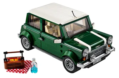 A green Lego MINI Cooper with a white roof, parked next to a picnic basket and a bottle of blue liquid on a red and white checkered blanket.