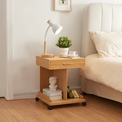 A bedside table with a lamp, plant, and books next to a bed.