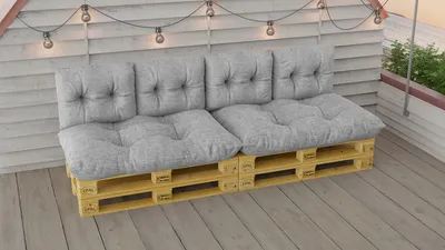 A pallet sofa with gray cushions on a wooden deck, decorated with string lights.