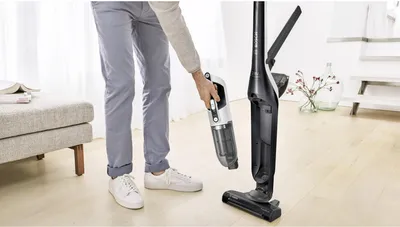 A person is holding a handheld vacuum cleaner and is about to attach it to a stick vacuum cleaner base.