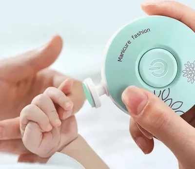 A close-up shot of a baby's finger being trimmed with an electric nail file.