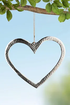 A silver heart-shaped ornament hangs from a tree branch against a blue sky.
