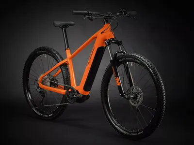 A studio shot of an orange electric mountain bike against a black background.