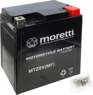 A black motorcycle battery with red terminal cover and silver connectors, shown on a white background. A small bag of screws and nuts is in the lower right corner.