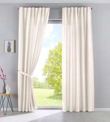 A room with a large window covered by cream-colored curtains. A small table with decorative items is placed to the left of the window.