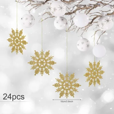 Gold glitter snowflakes and white Christmas ornaments hang from a branch against a blurred snowy background.