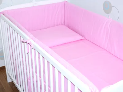 A close-up view of a pink baby crib bedding set, including a bumper and a pillow, inside a white crib.