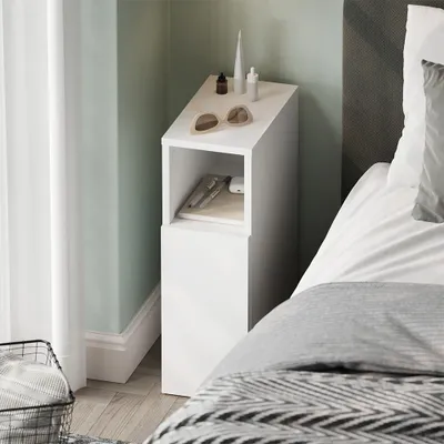 A white bedside table with items on top and inside, next to a bed.