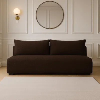 A dark brown boucle sofa is shown in a well-lit room with white paneled walls and a round mirror above it. A light-colored rug is in the foreground.