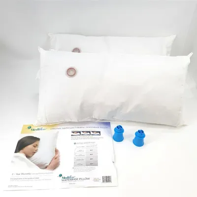 Two white pillows are shown on a white background, with a product information sheet and two blue caps in the foreground.