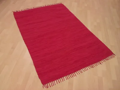 A red rug with fringe on a wooden floor.