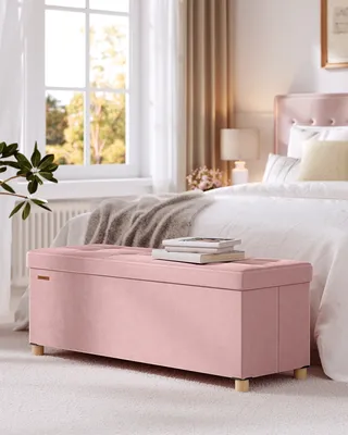 A pink storage bench is placed in front of a bed in a bedroom setting.