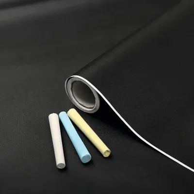 A roll of black chalkboard contact paper with three pieces of chalk in white, blue, and yellow.