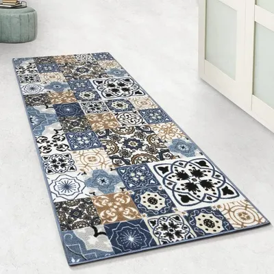 A runner rug with a mosaic tile pattern is laid out on a light-colored floor, next to a white cabinet.