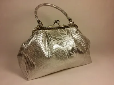 A silver handbag with a floral pattern is displayed against a light gray background.