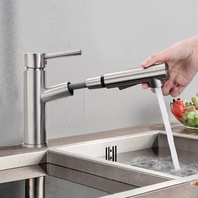 A hand is using a pull-out kitchen faucet to spray water into a sink, with a bowl of fruit in the background.