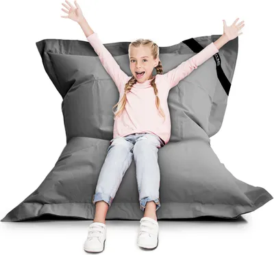 A young girl is sitting on a large grey beanbag chair with her arms raised in excitement.