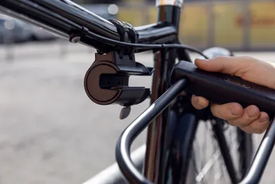 A hand is holding a black bicycle lock near the handlebars of a black bicycle.