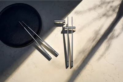 A set of chopsticks and a chopstick rest are arranged on a textured surface with dramatic shadows.