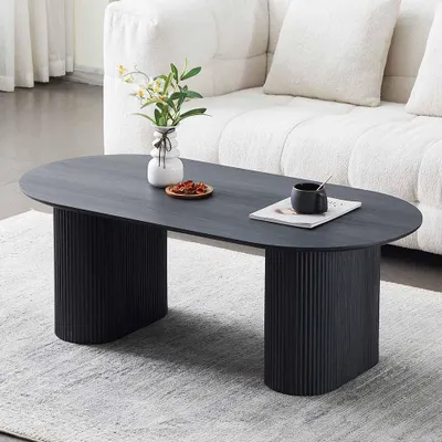 A black oval coffee table with fluted legs sits on a light gray rug in front of a white sofa.